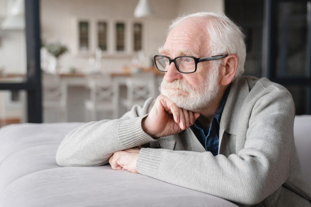 An older man in need of geriatric behavioral health treatment stares out a window.