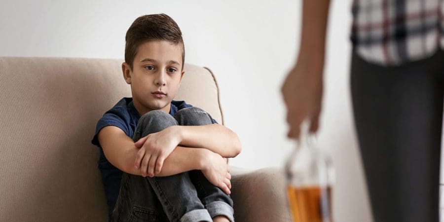 Kid sitting on the couch looking at alcohol drinking on his parents hand